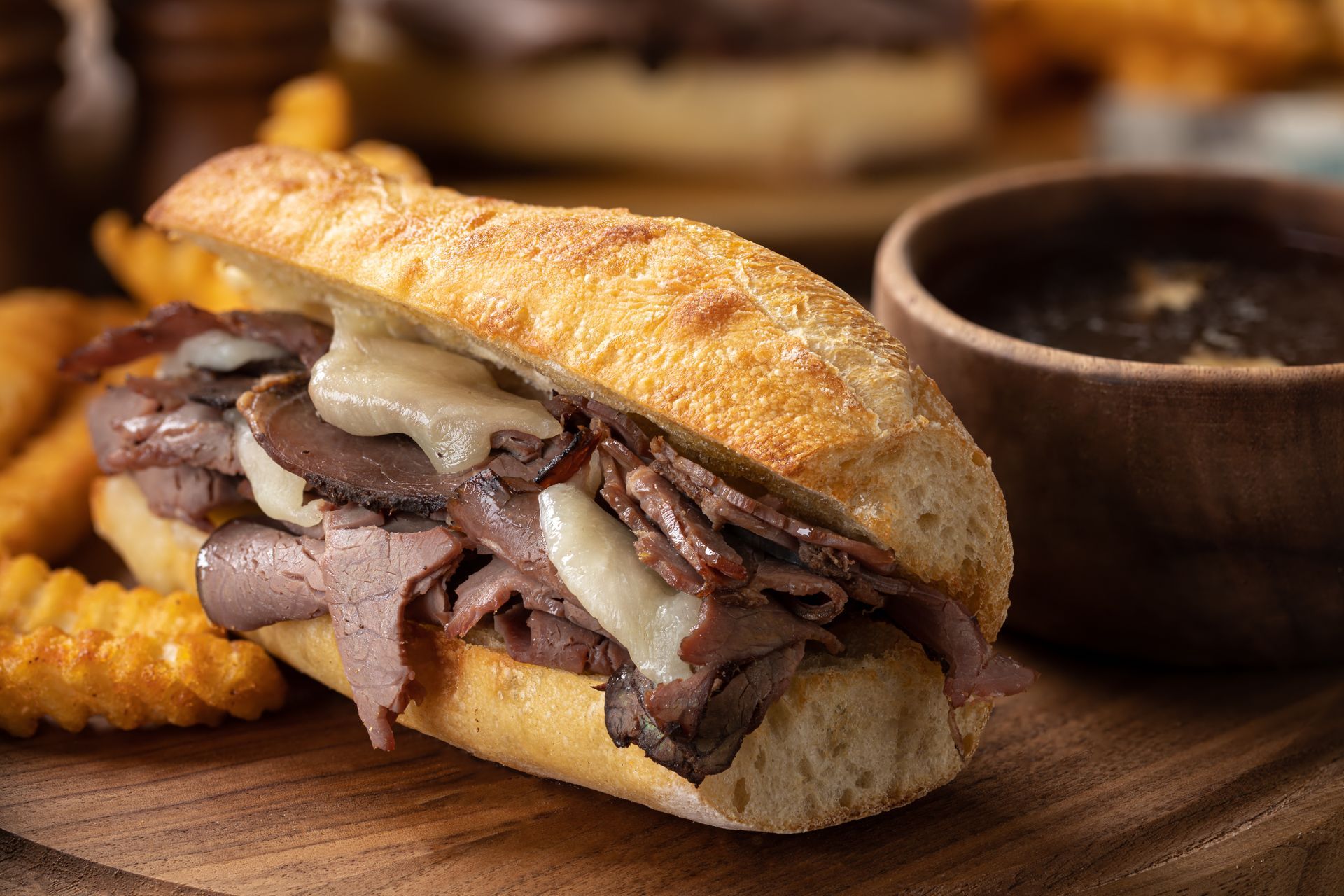 A roast beef sandwich and french fries on a wooden cutting board.