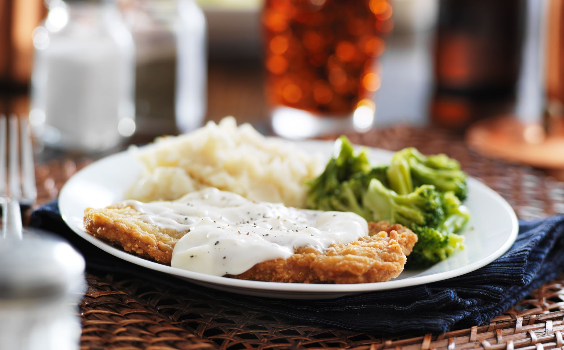 A plate of chicken fried steak with gravy , mashed potatoes and broccoli on a table.