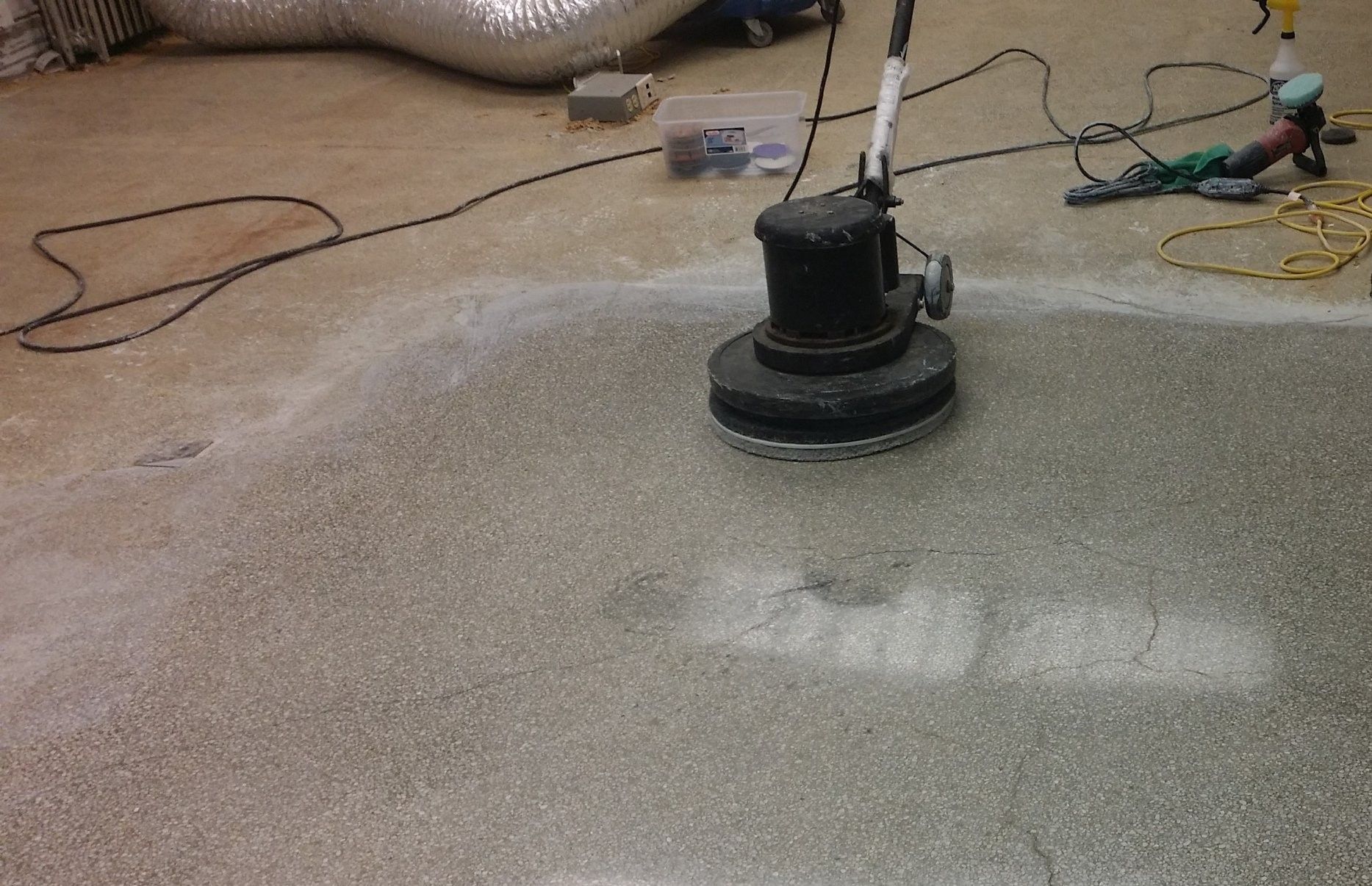 Floor-cleaning machine scrubbing a wet concrete surface indoors