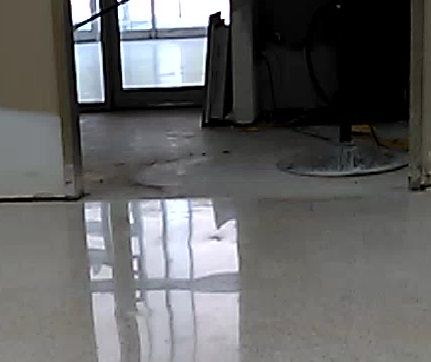 Empty indoor room with glossy floor reflecting windows and a doorway in the background