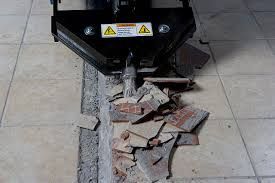 A black tool breaking concrete pavement, with broken bricks and debris scattered below.