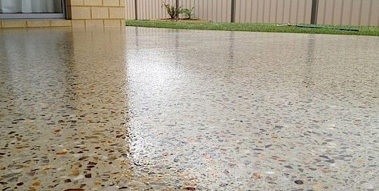 Rainwater pooling on a speckled concrete patio beside a beige building and metal fence