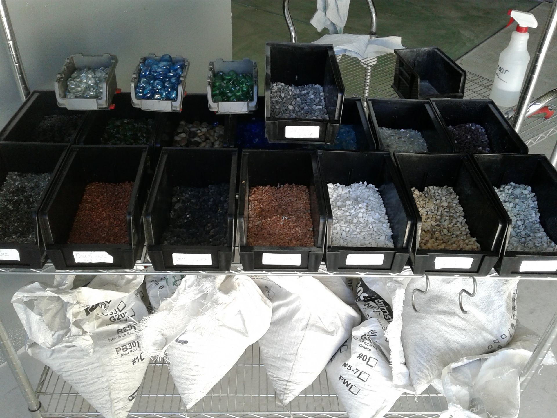 Assorted bins of beans, seeds, and supplies arranged on a table with white sacks in front.