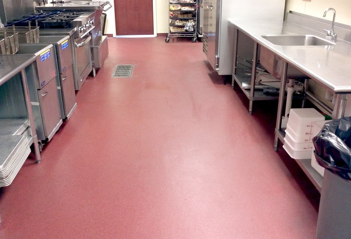 Commercial kitchen aisle with stainless steel counters, sinks, and red flooring