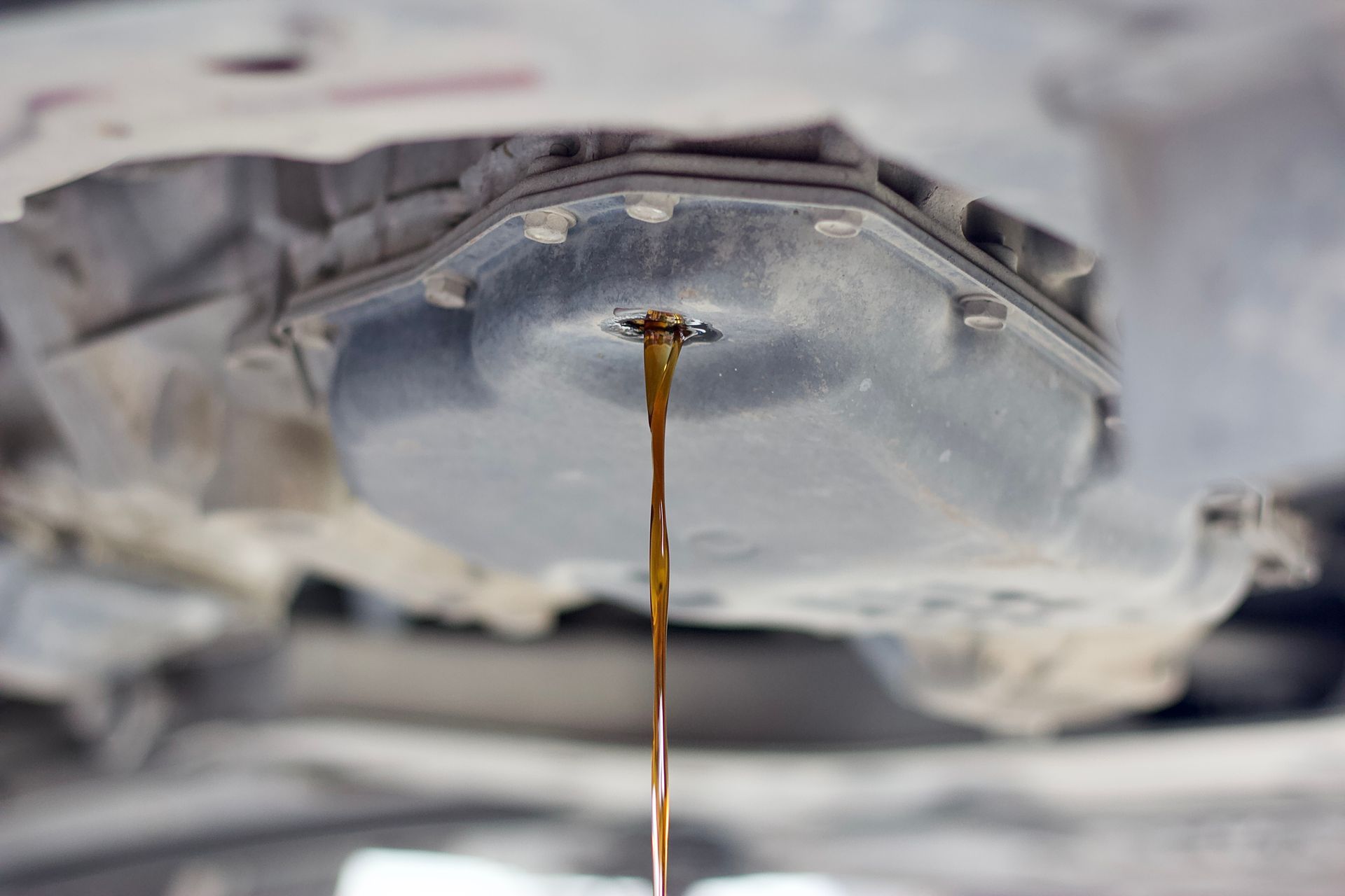 Close-up of dark oil dripping from a car engine drain plug into a container