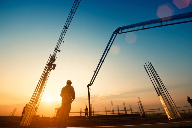A Man Is Standing In Front Of A Construction Site At Sunset — Lonnie Henderson Concreting In Kurri Kurri, NSW