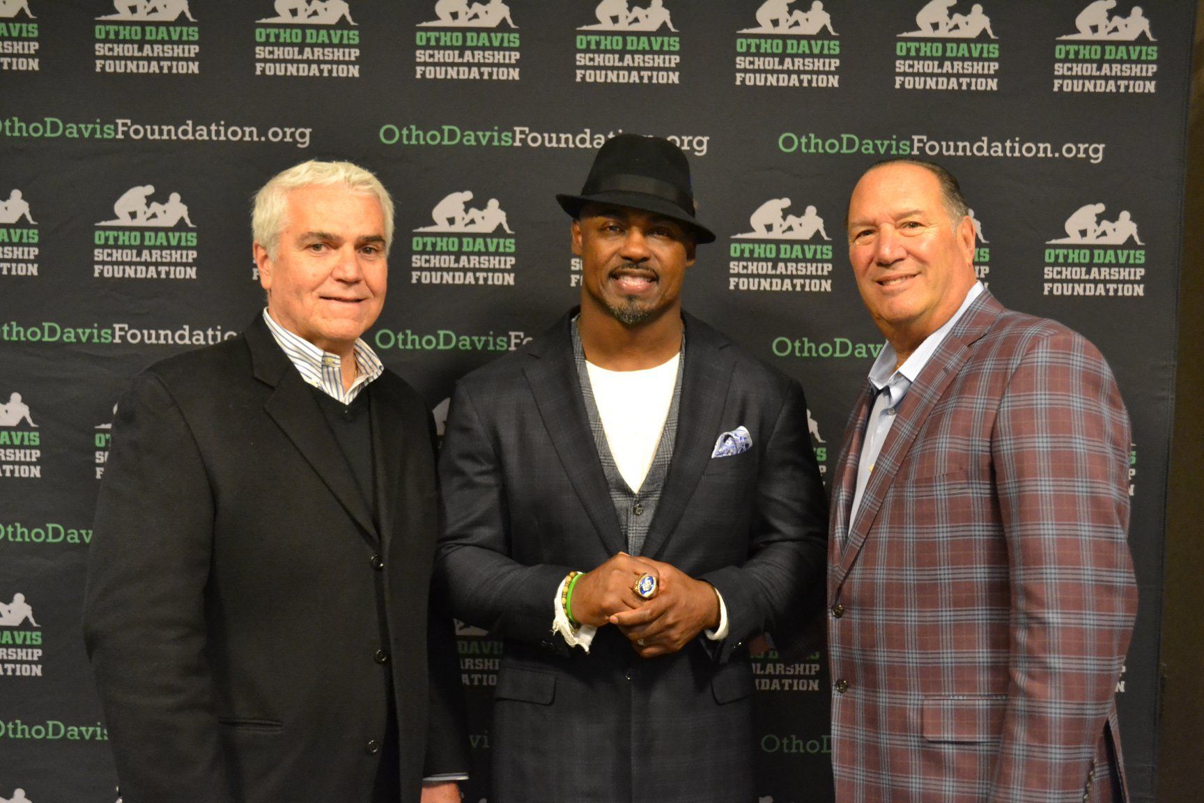 Three men are posing for a picture in front of a wall that says the davis foundation