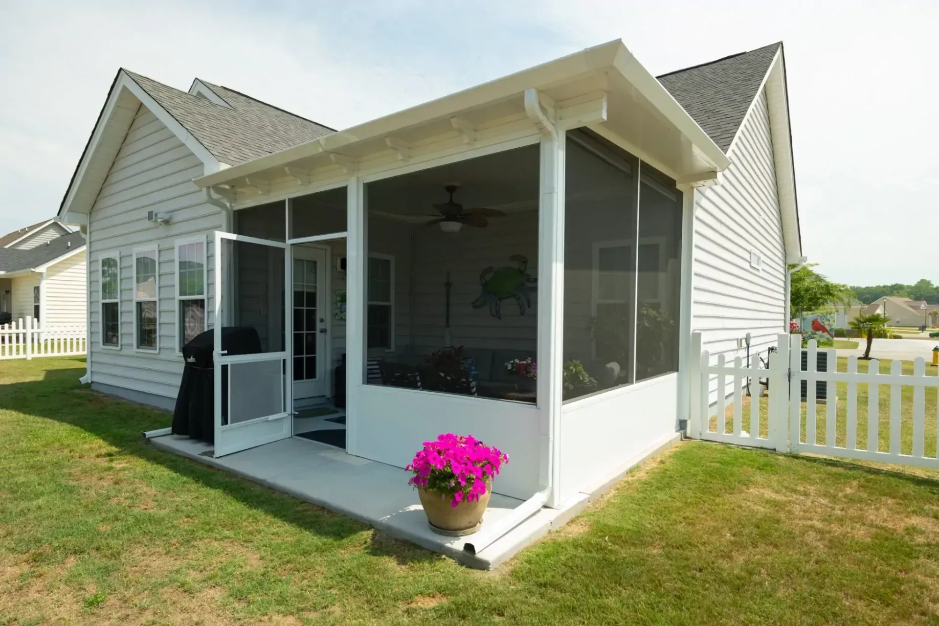 A side view of a house featuring a white-framed screened porch with a pink potted plant on the patio.