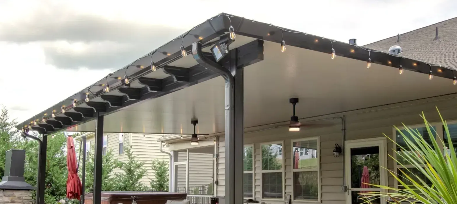 A covered patio area attached to a house featuring a dark metal structure, ceiling fans, and string lights.