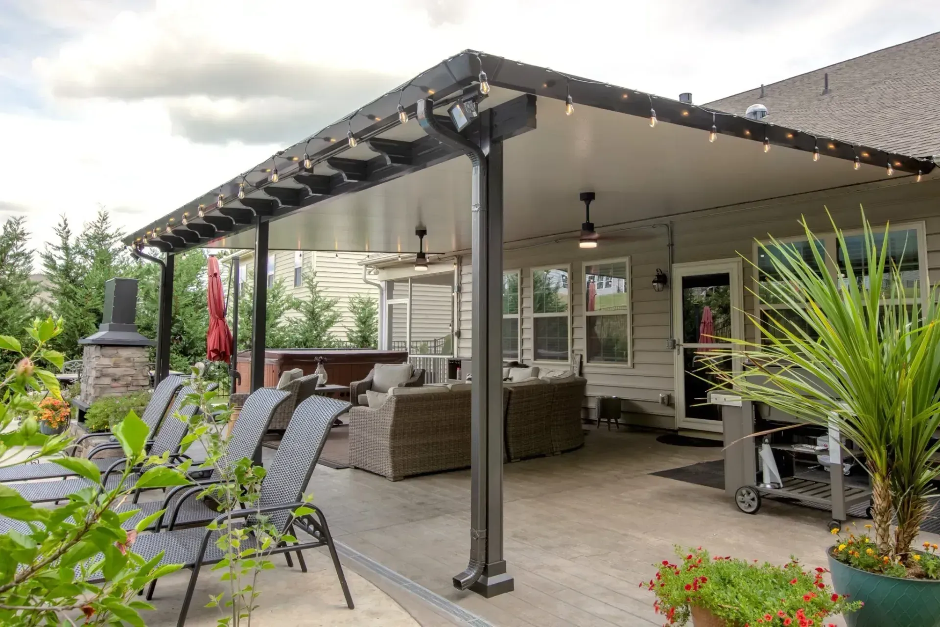 A patio featuring an outdoor covered seating area with wicker furniture, a ceiling fan, and lounge chairs on a deck.
