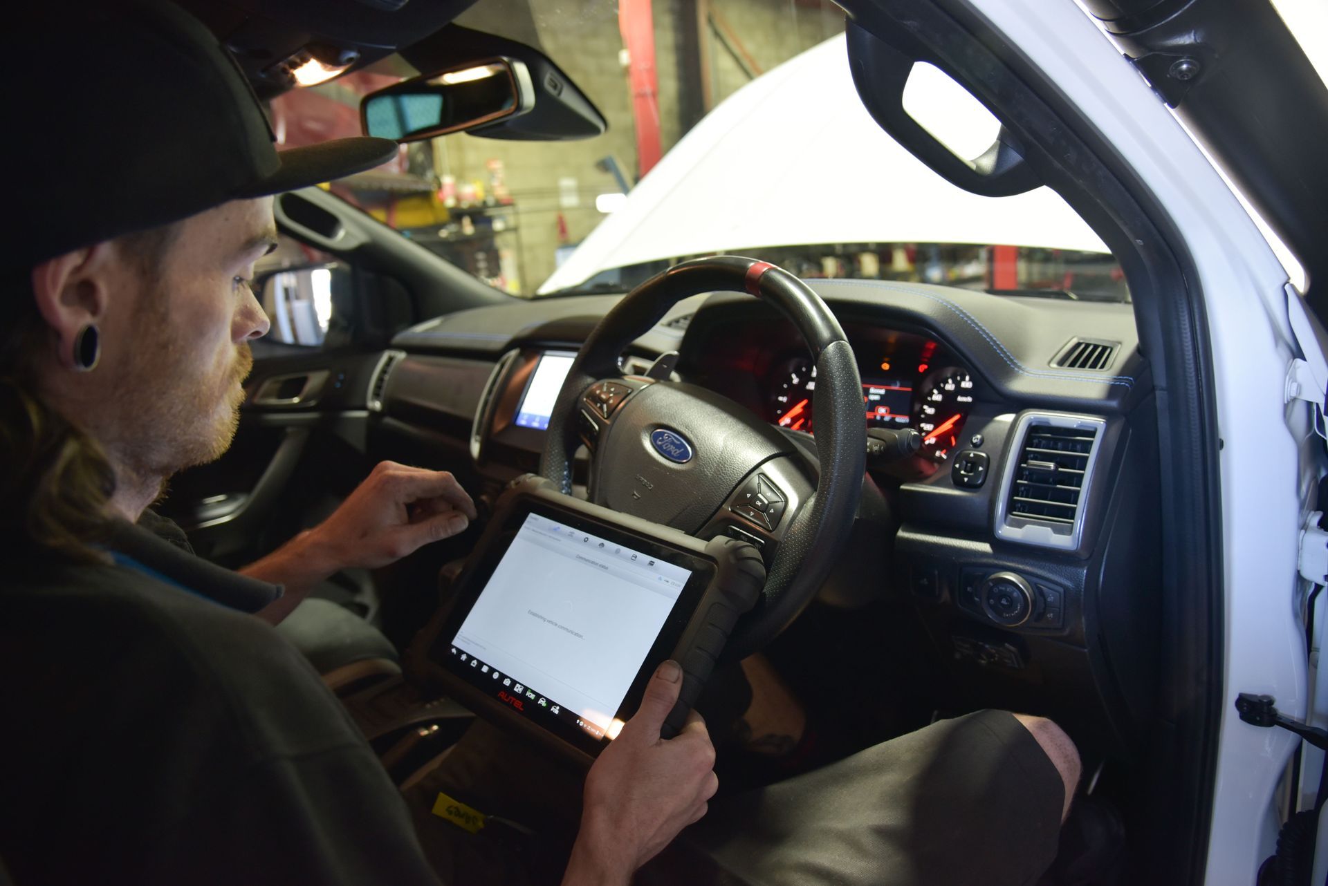 A man is sitting in the drivers seat of a car running tests on a machine  — Advanced Automotive Services in Coffs Harbour, NSW