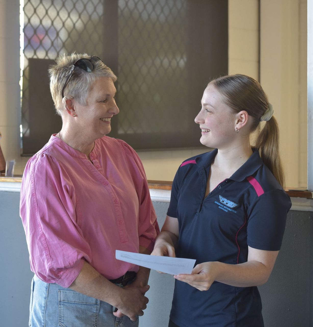 Two ladies are standing at a reception discussing an invoice together while smiling — Advanced Automotive Services in Coffs Harbour, NSW