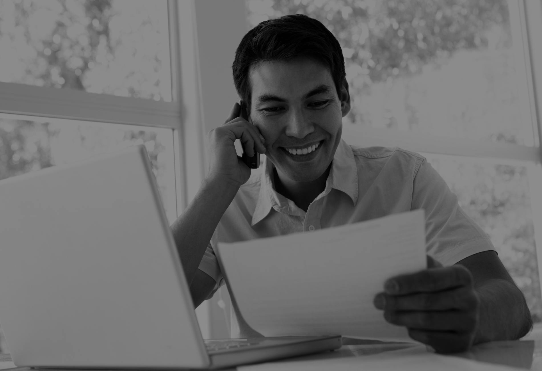 A man is talking on a cell phone while looking at a piece of paper.