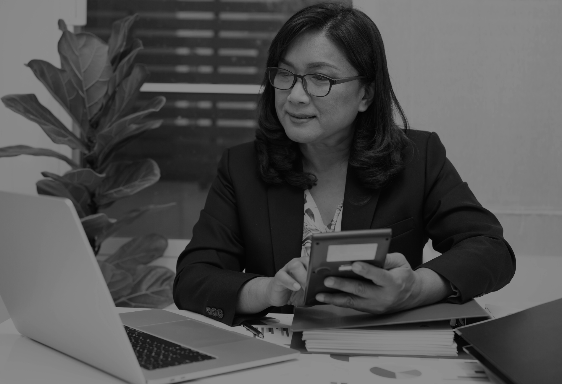 A woman is sitting at a desk holding a calculator and a cell phone.