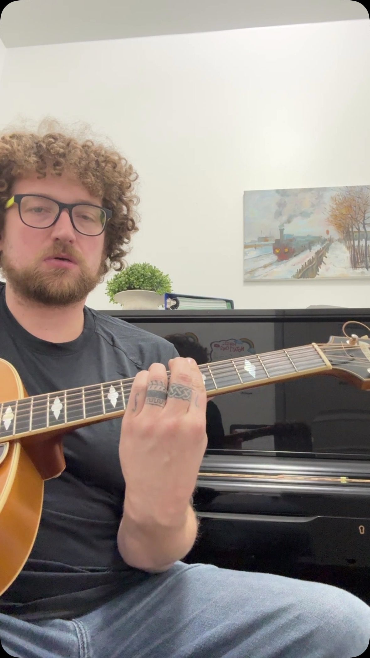A man with curly hair is playing a guitar in front of a piano.
