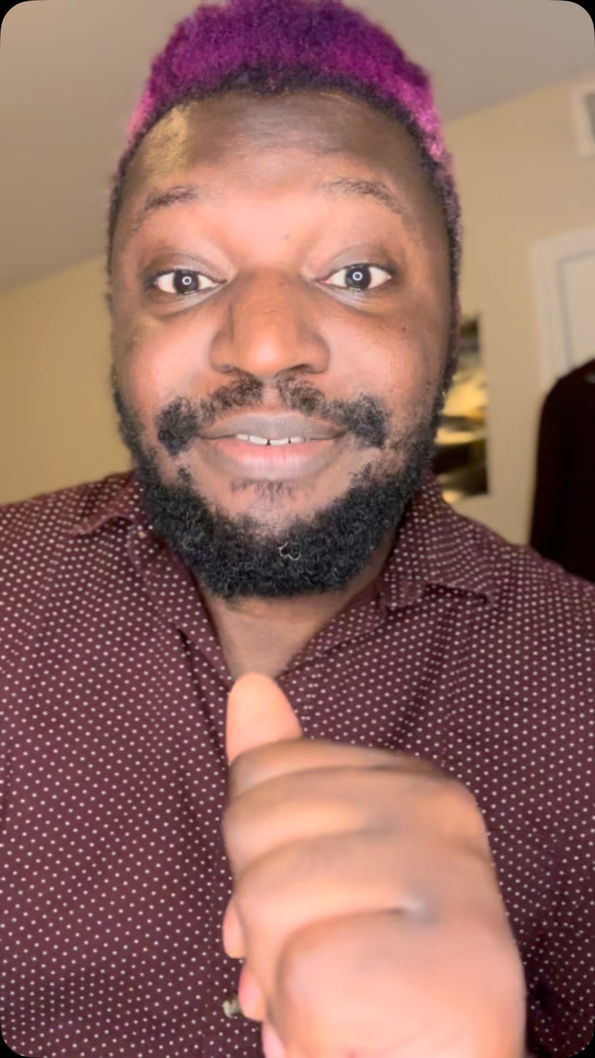 A man with purple hair and a beard is giving a thumbs up.