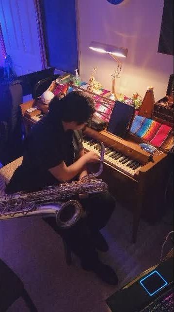 A man is playing a saxophone in front of a piano.