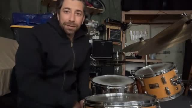 A man is standing in front of a drum set in a garage.