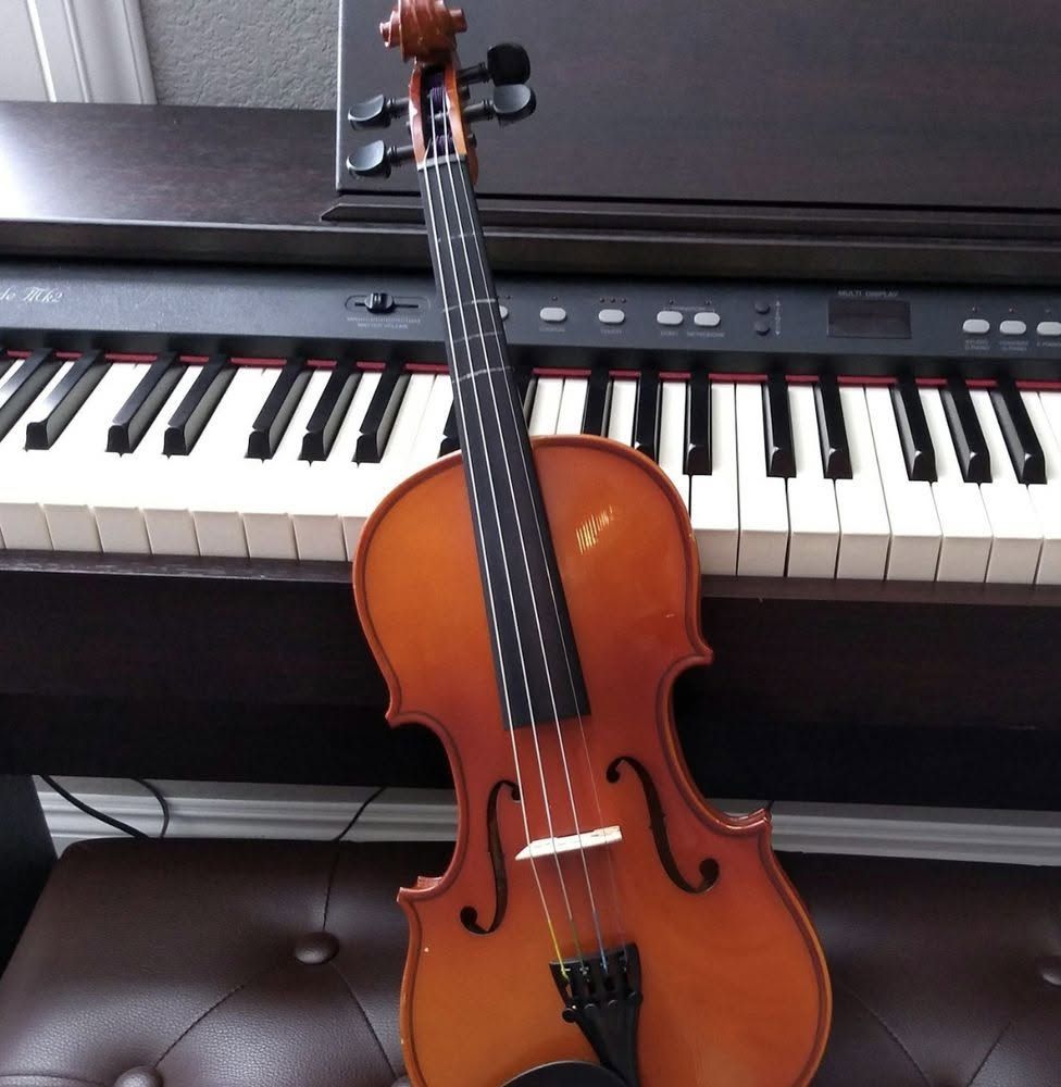 Violin leaning against a black digital piano on a dark bench