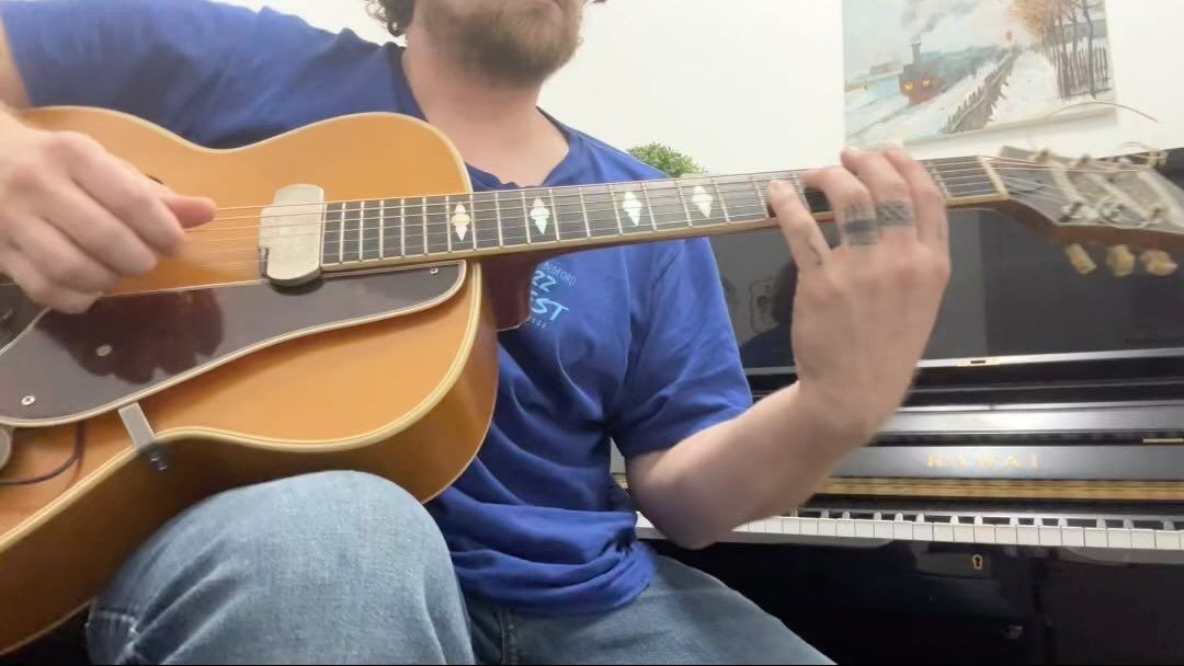A man is playing a guitar in front of a piano.