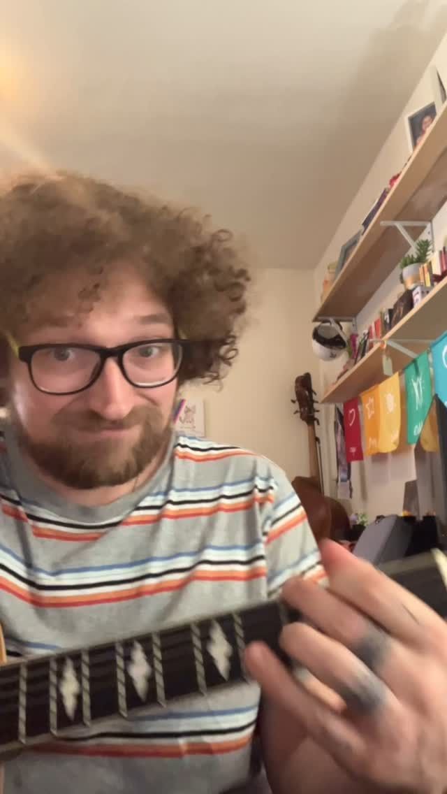A man with curly hair and glasses is holding a guitar