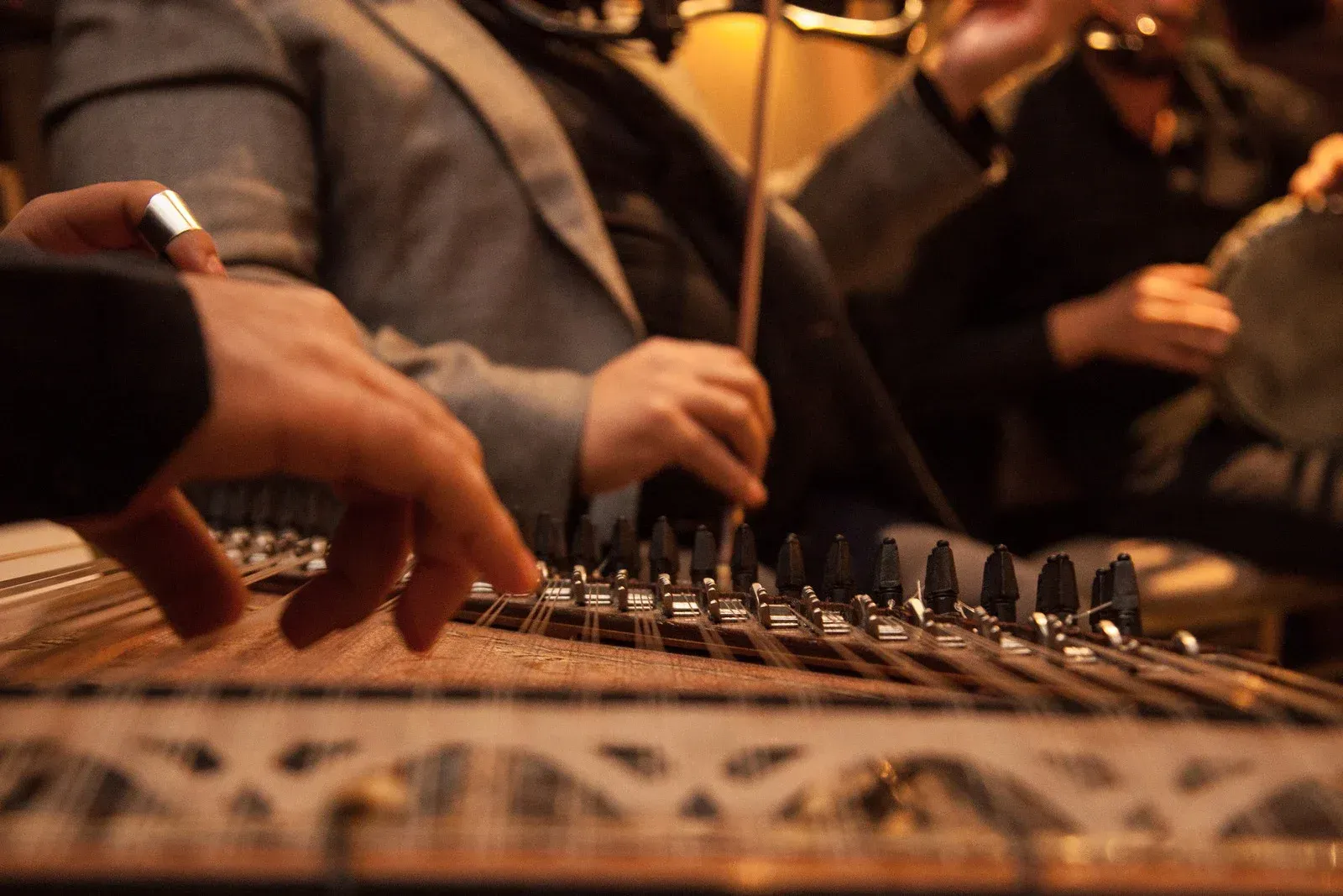 Hands playing a qanun, a stringed instrument. Musicians perform in a dimly lit setting.