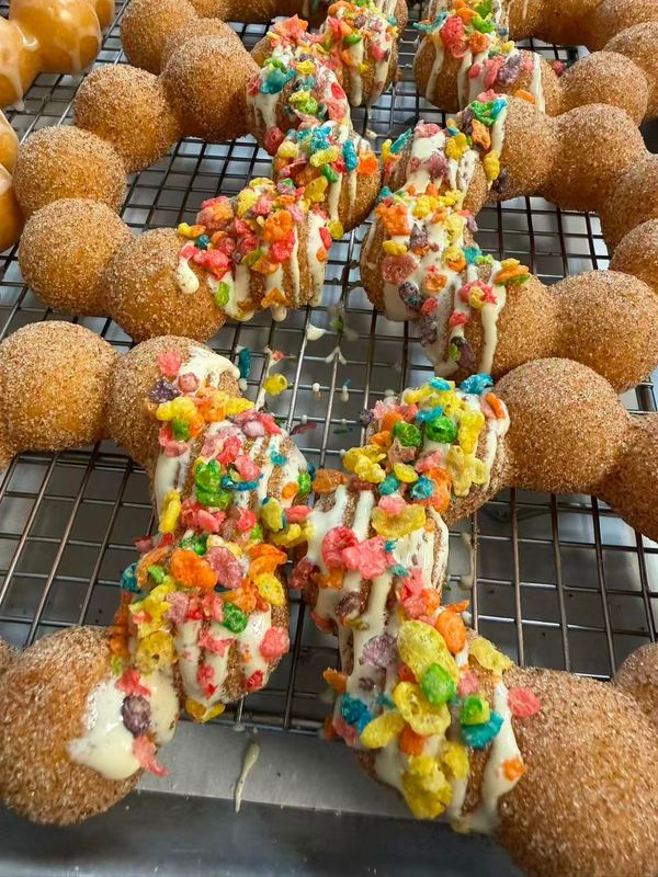 A tray of six colorful mochi-style donuts arranged in two rows of three on parchment paper against a tan background.
