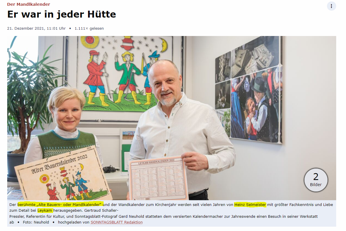 Zwei Personen halten Plakate in einer Kunstgalerie hoch; im Hintergrund sind farbenfrohe Kunstwerke und ein großes Wandgemälde zu sehen.
