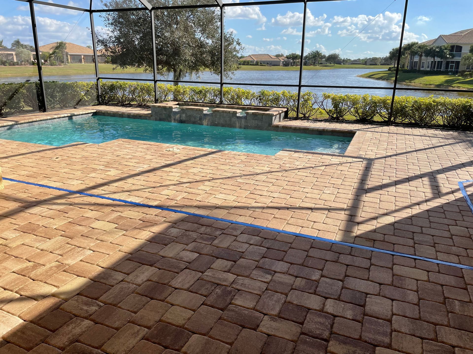 Paver pool deck inside a screened enclosure overlooking a lake.