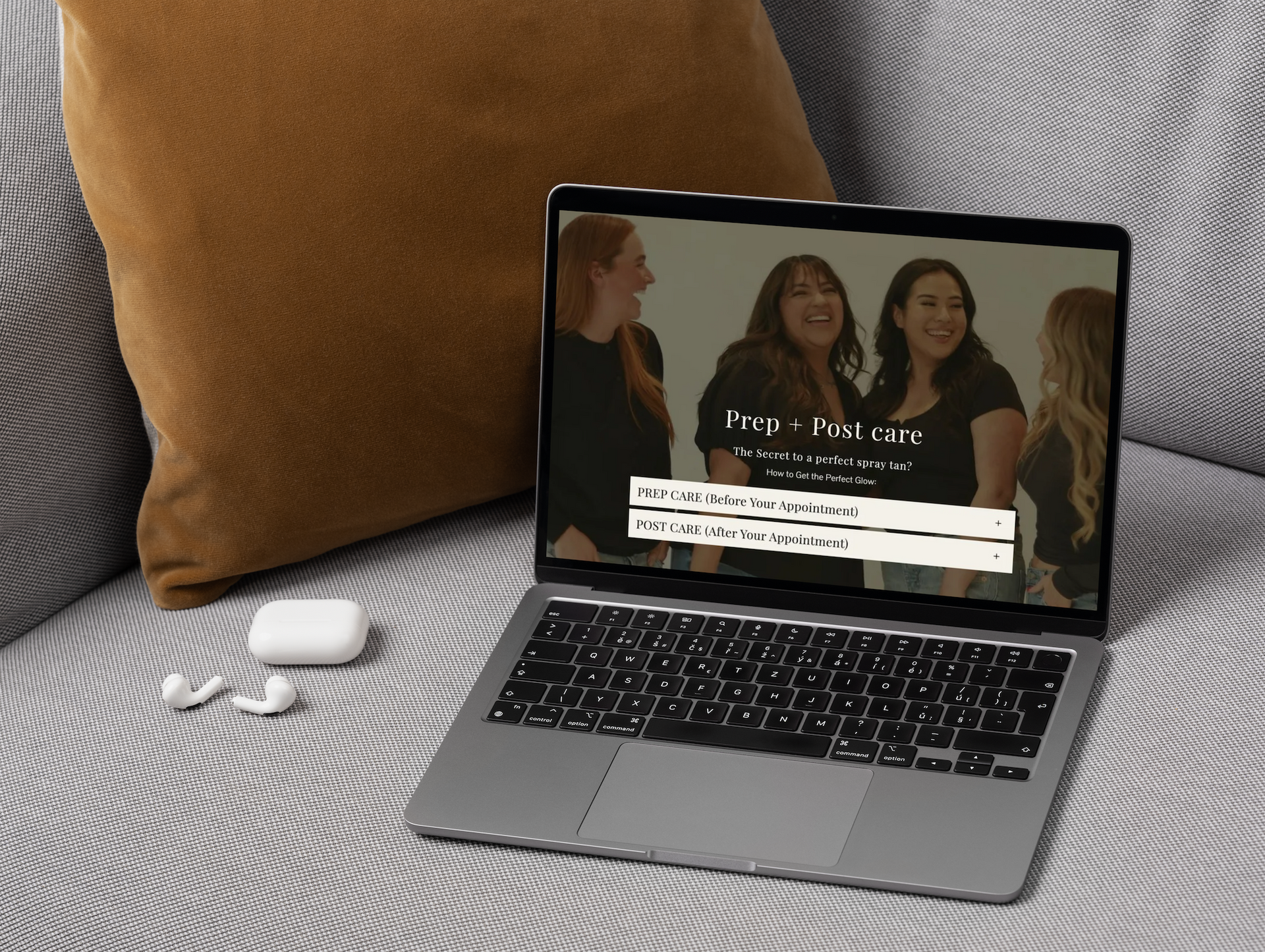 Laptop on a bed showing a website, with a tan pillow and white earbud case nearby.