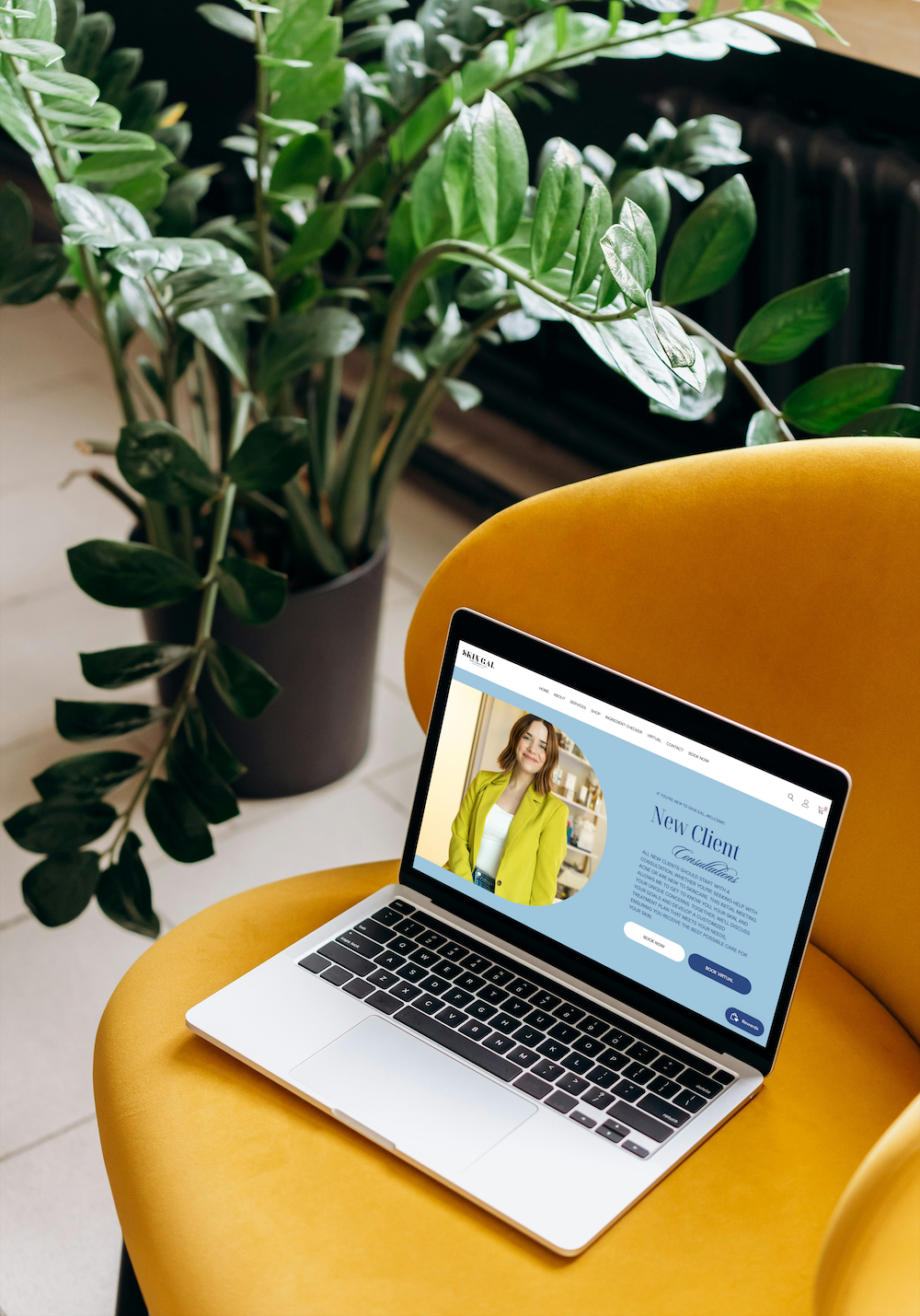 Laptop open on a yellow chair beside a potted plant, showing a website on its screen