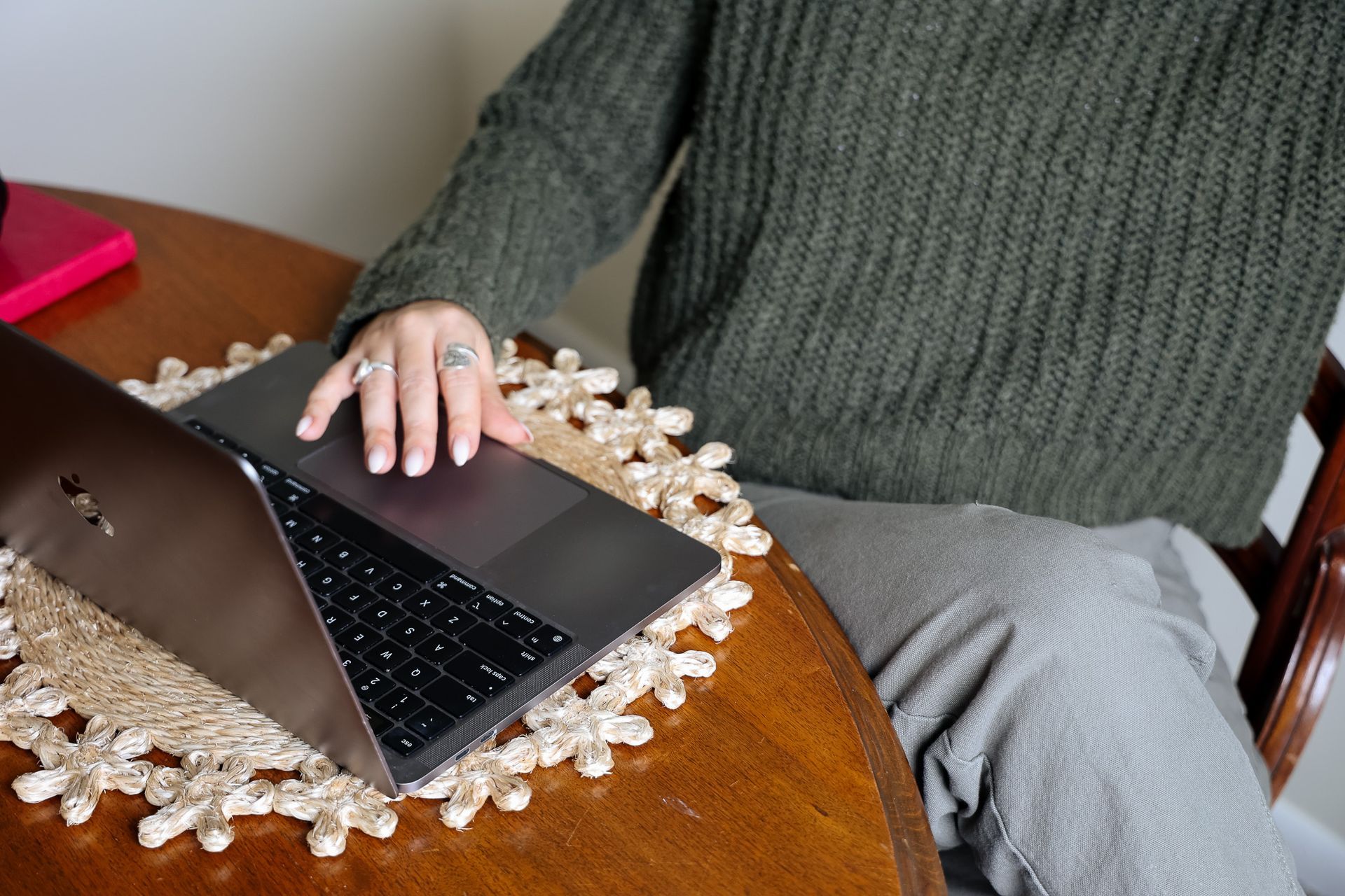 Person using a laptop at a wooden table with a lace doily and green sweater