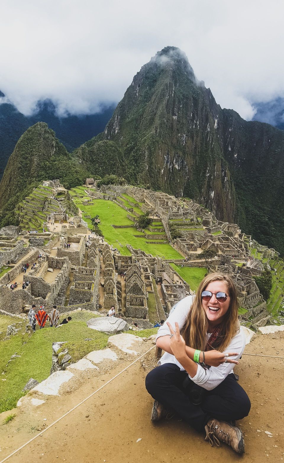 Woman crouching on a mountain overlook with Machu Picchu and misty peaks in the background