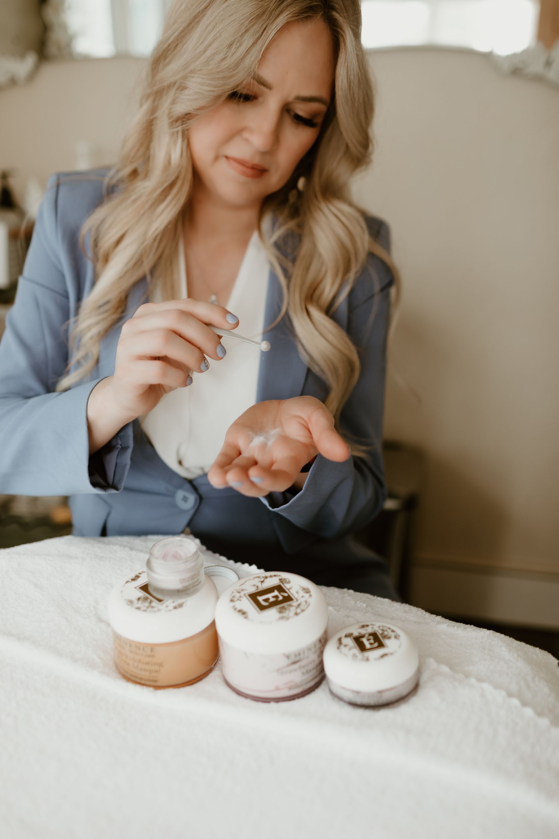 Woman decorating small iced cakes with a piping bag on a table covered in white fabric