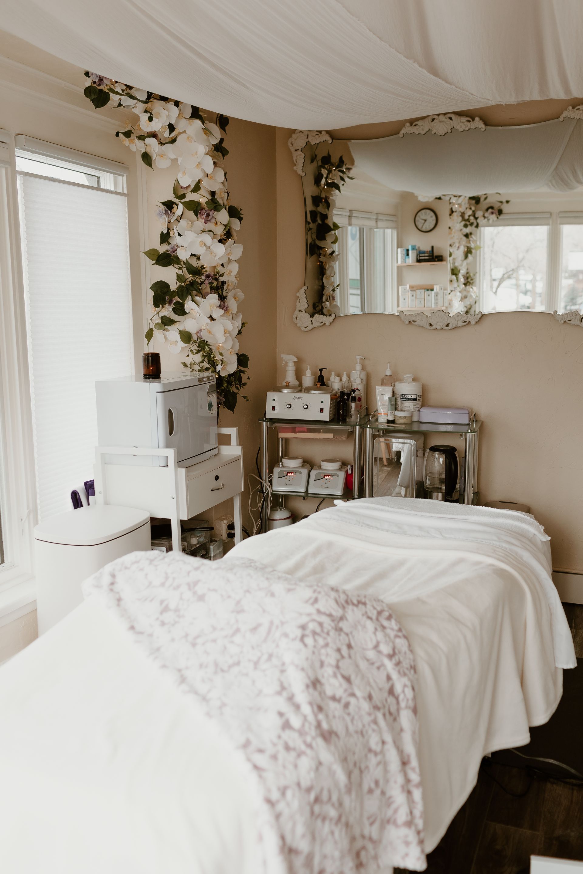 Cozy beige spa room with treatment bed, vanity, mirror, and floral decor