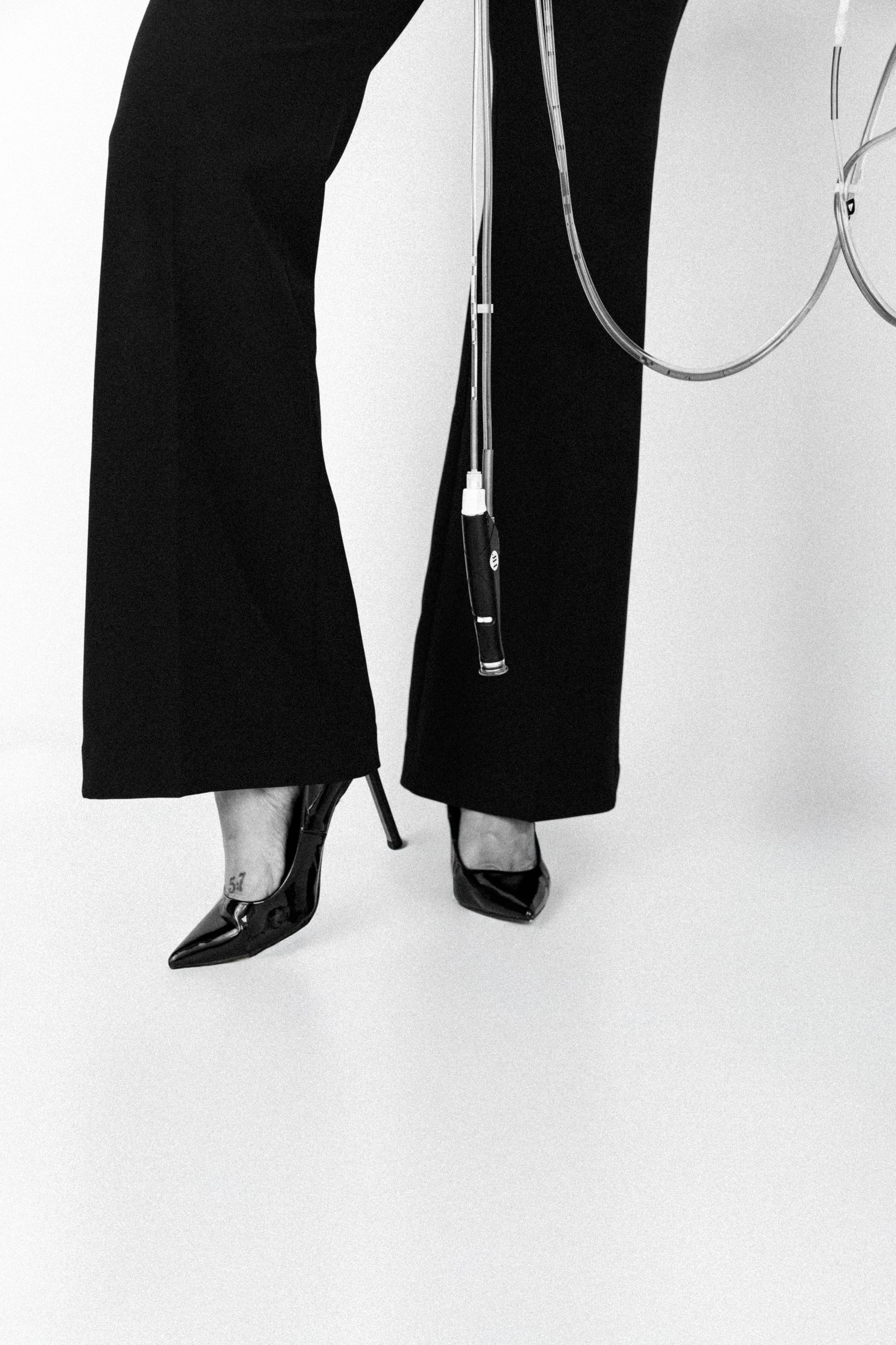 Black flared pants and shiny heels on a white studio background, with a handbag chain visible.