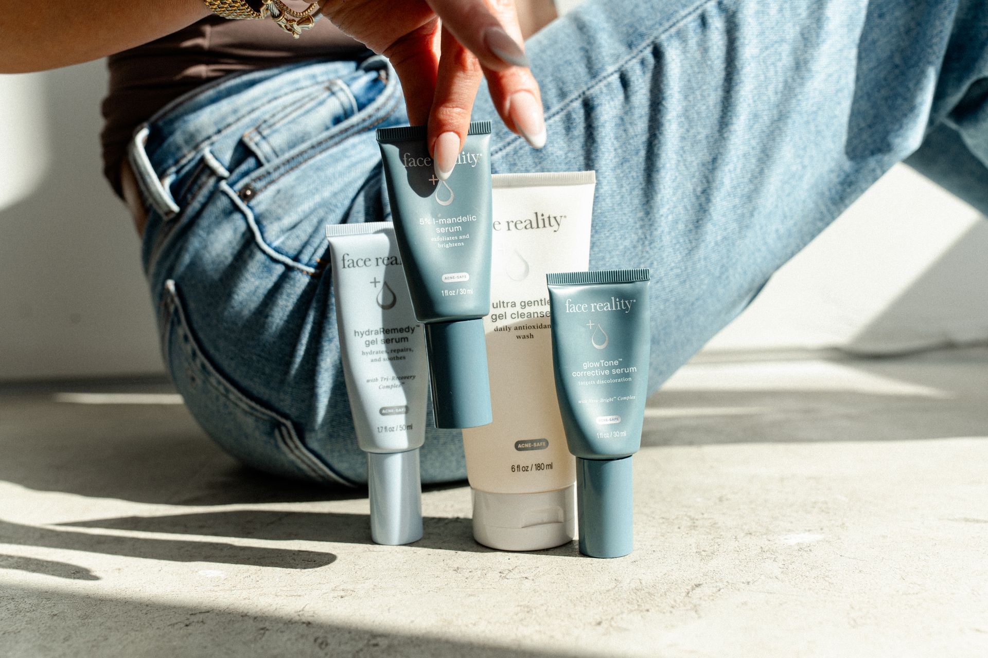 Blue jeans, a seated person, and four skincare tubes on a sunlit floor.