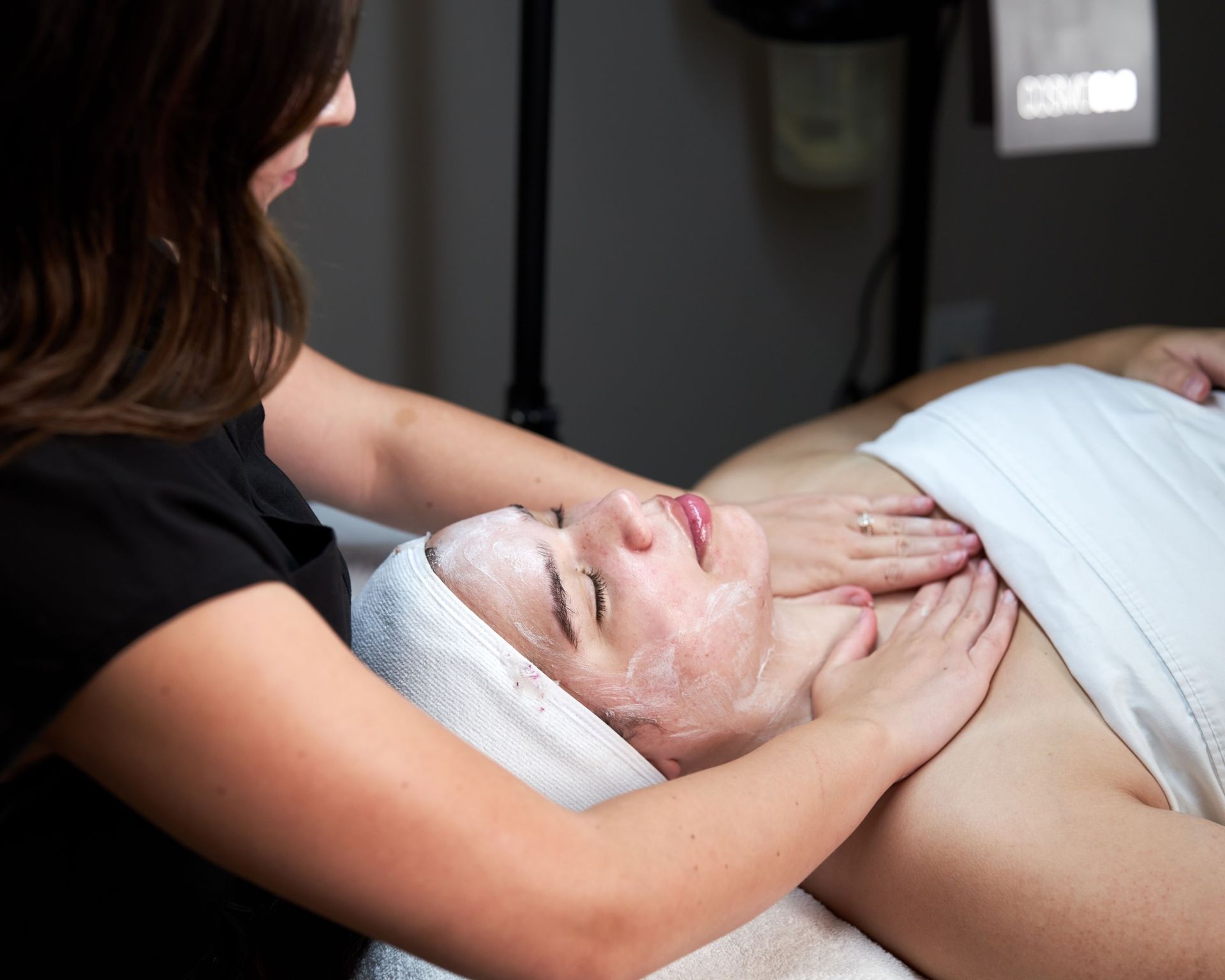 Spa facial treatment with a woman massaging a client’s face with a cream mask and head wrap
