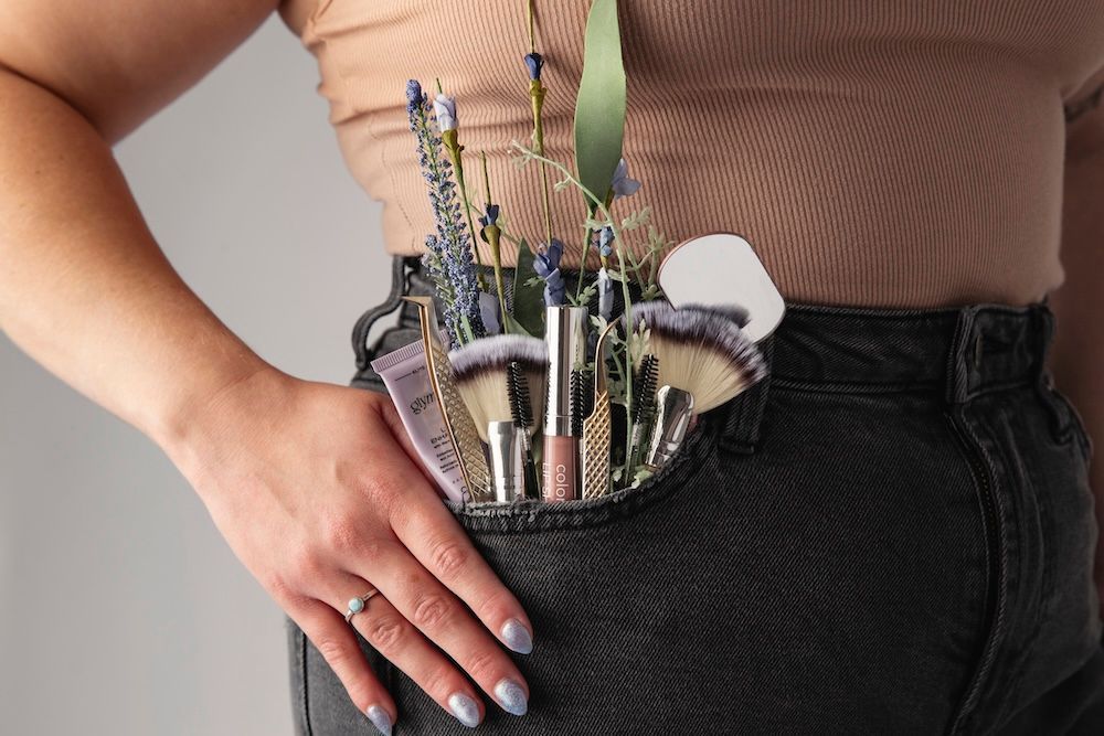 Person holding a black waist pouch filled with makeup brushes and lipsticks