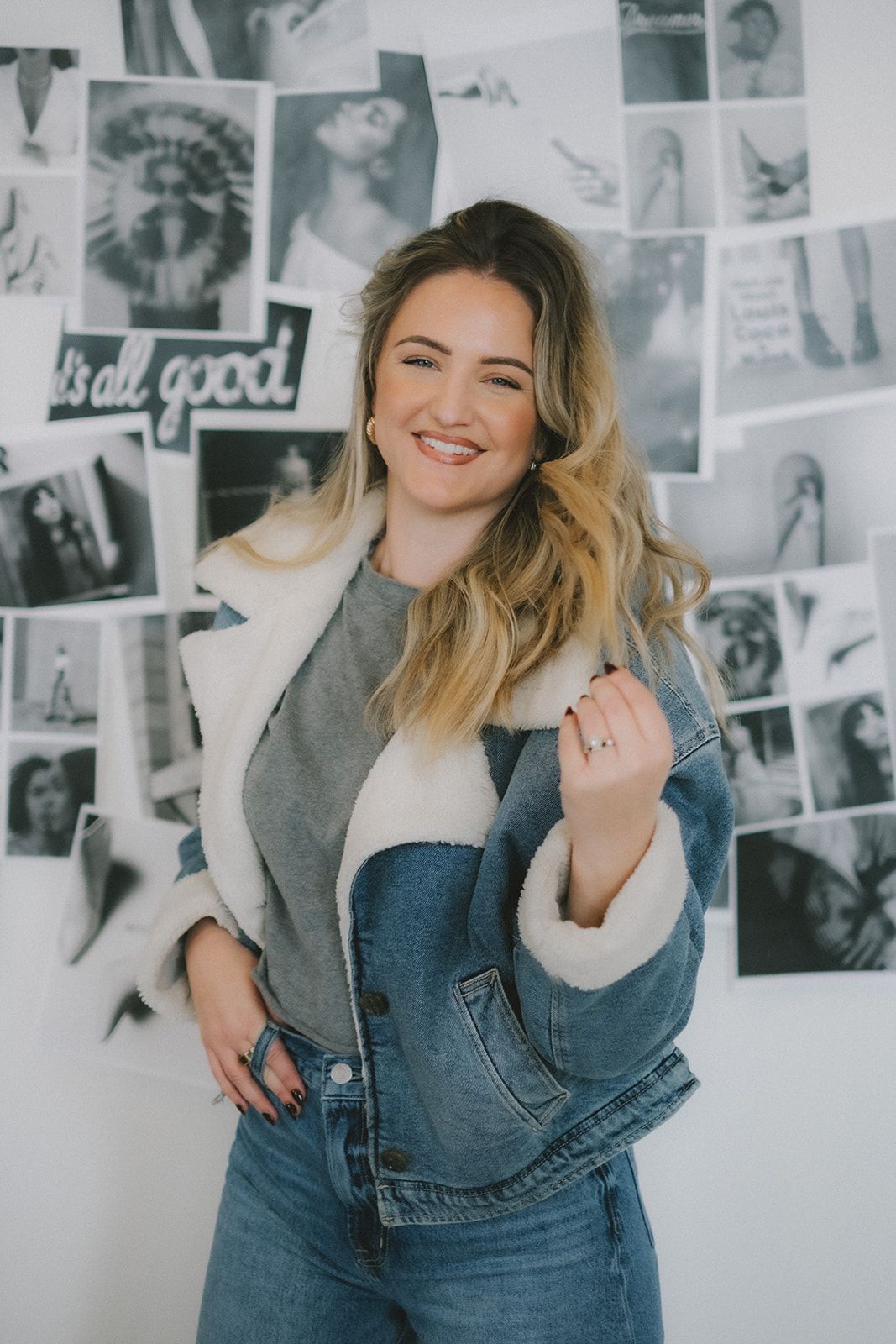 Smiling woman in denim jacket standing before a black-and-white photo wall