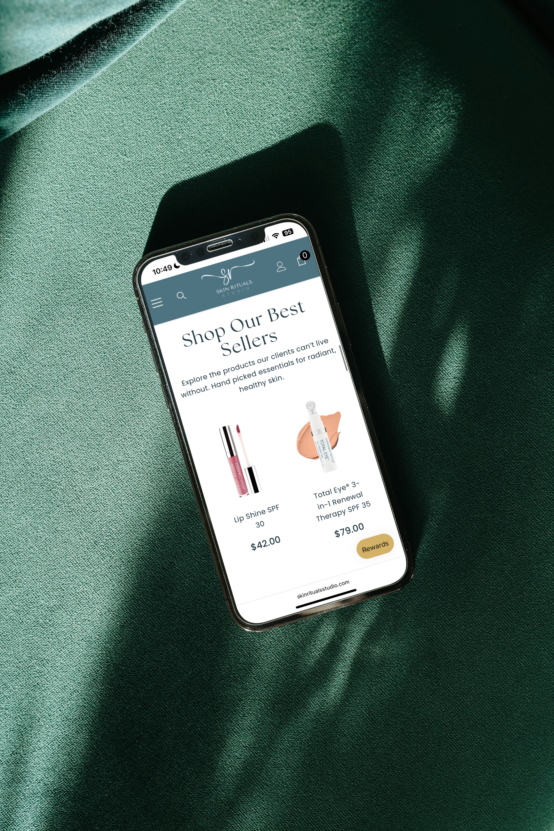 A smartphone displaying a product page with skin care items lies on a green textured fabric.