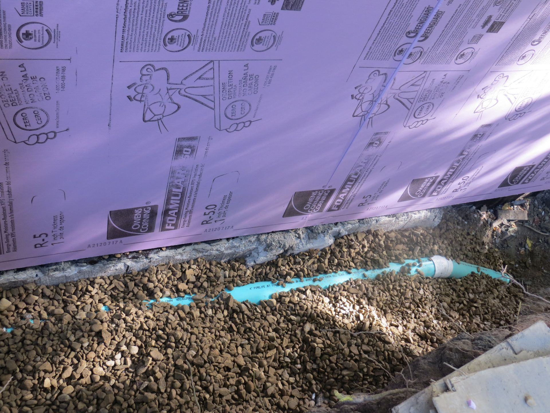 Purple insulation panel, gray gravel, and a turquoise pipe.