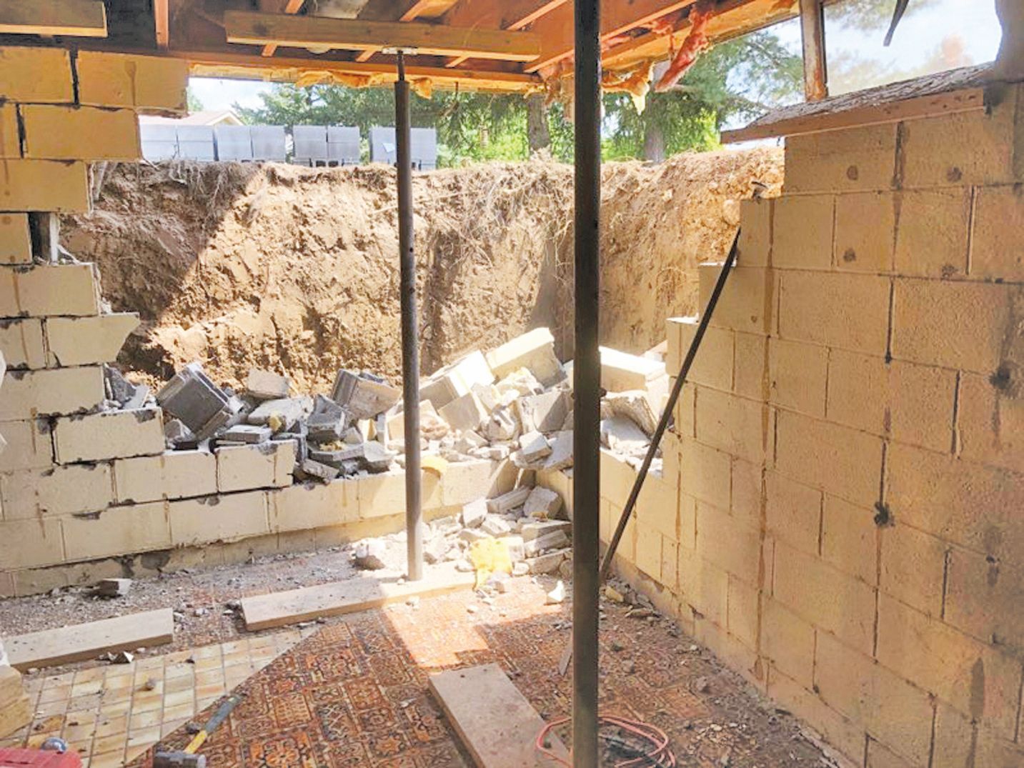 Construction site: partially demolished concrete block walls, dirt excavation, support beams.