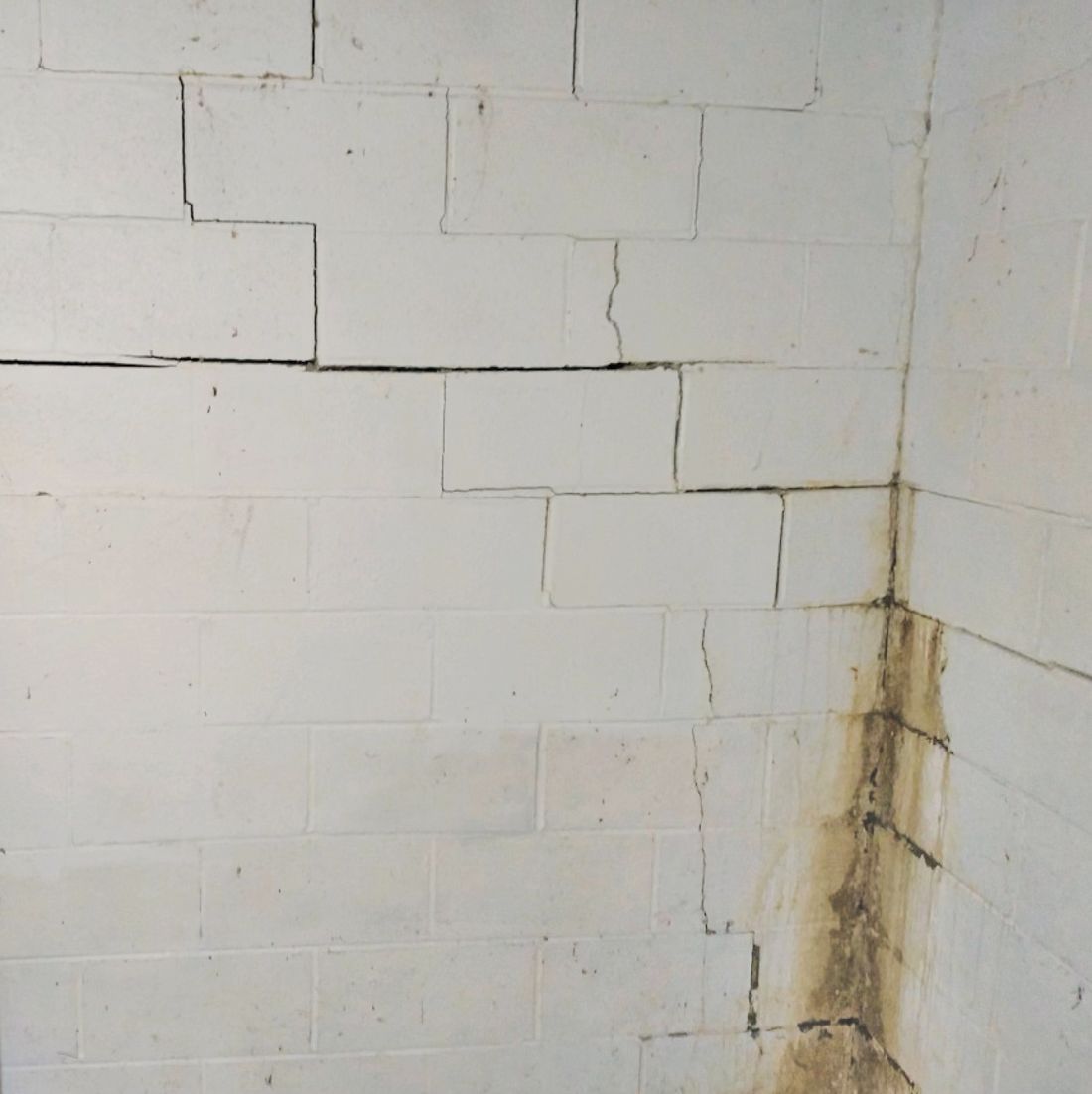 White cinder block wall with cracks and water stains in the corner.
