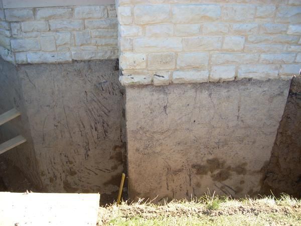 Foundation of a stone building exposed by an excavation, showing soil and structure.