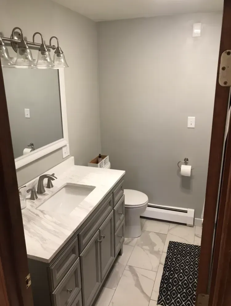 Bathroom with gray walls, white vanity, marble-look floor, toilet, and a small black rug.