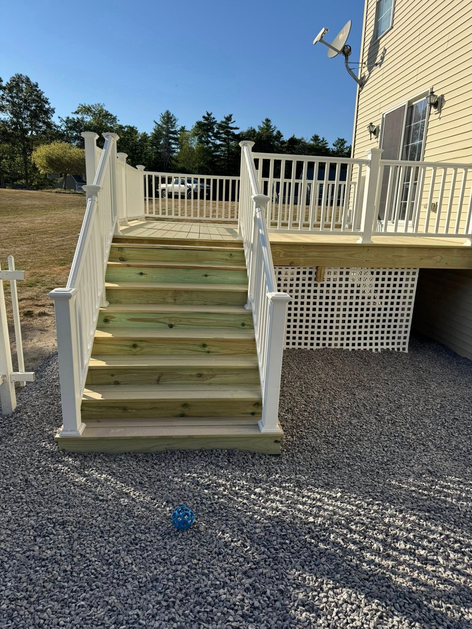 Wooden deck with stairs and white railing; gravel ground.