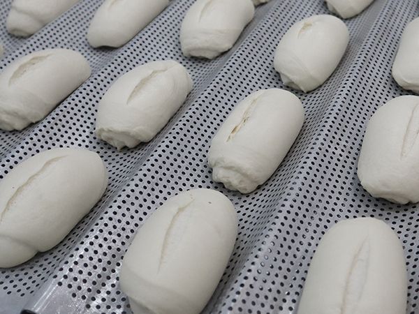 Un montón de panecillos blancos están sobre una bandeja perforada.