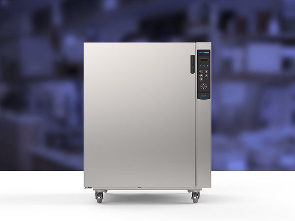 Un refrigerador de acero inoxidable con ruedas está sobre una mesa blanca.