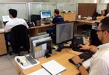 Un grupo de hombres están sentados en escritorios en una oficina trabajando con computadoras.